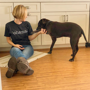 Girl sitting on the floor in boots and a tshirt that says 'ohana petting her brown dog