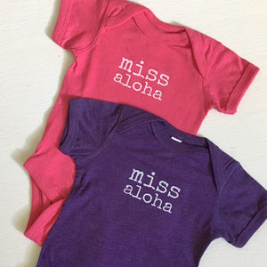 pink and purple baby girl onesie with white lettering that says miss aloha