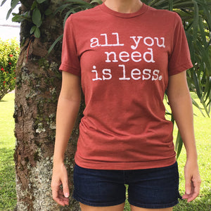 girl wearing jean shorts and gender neutral red t-shirt with white font that says all you need is less